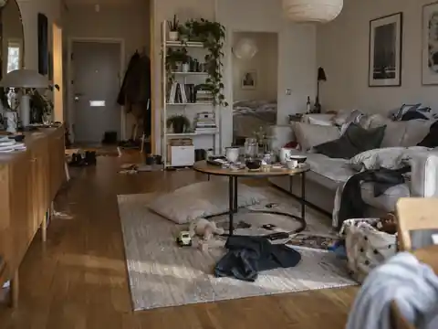 Vardagsrum före städning med oordning på golv, bord och soffa